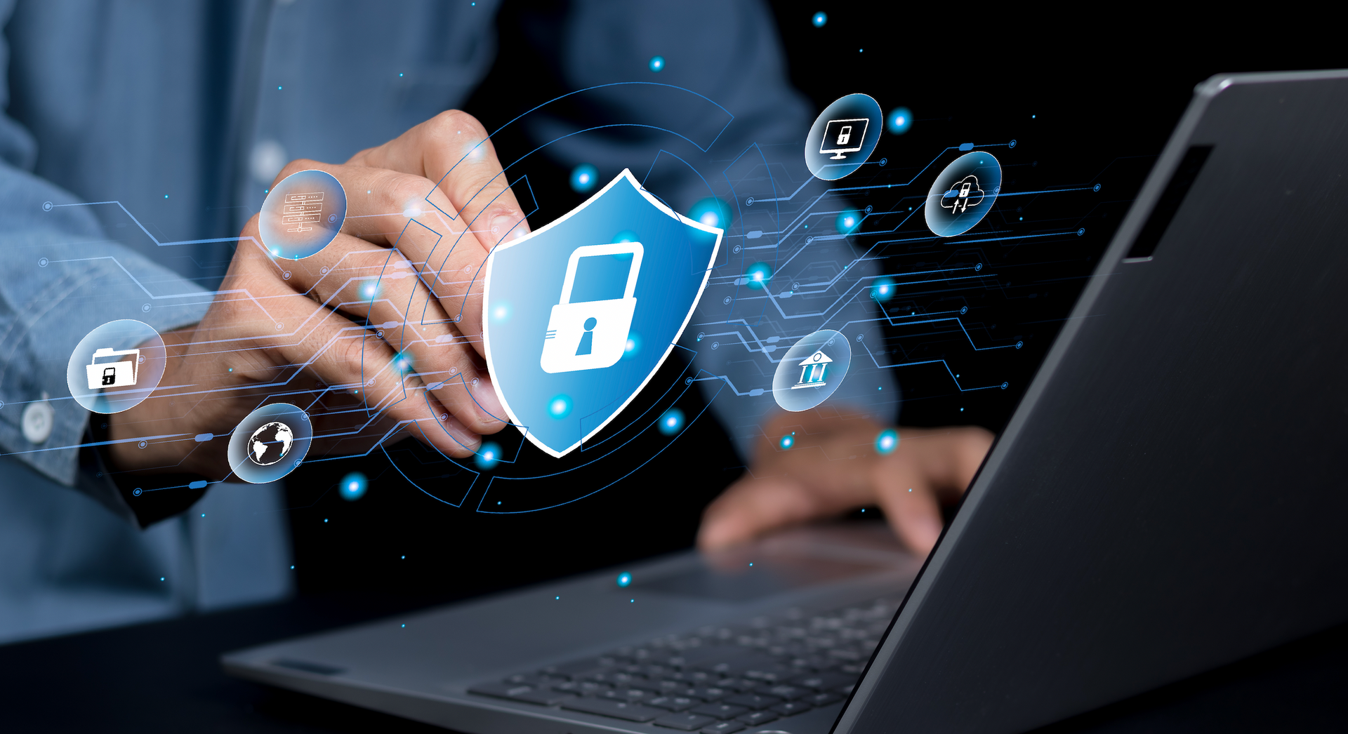 A person is holding a shield with a padlock on it in front of a laptop computer.