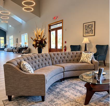 Modern lobby with curved gray sofa, patterned rug, side table, lamps, and floral arrangement.
