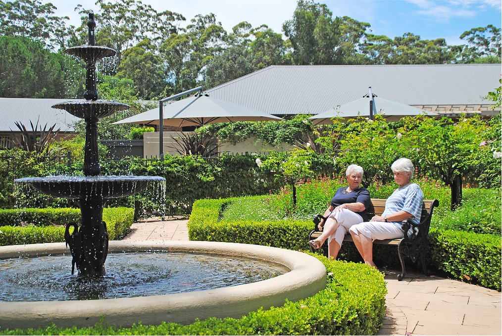 Two women sit on a bench in front of a fountain