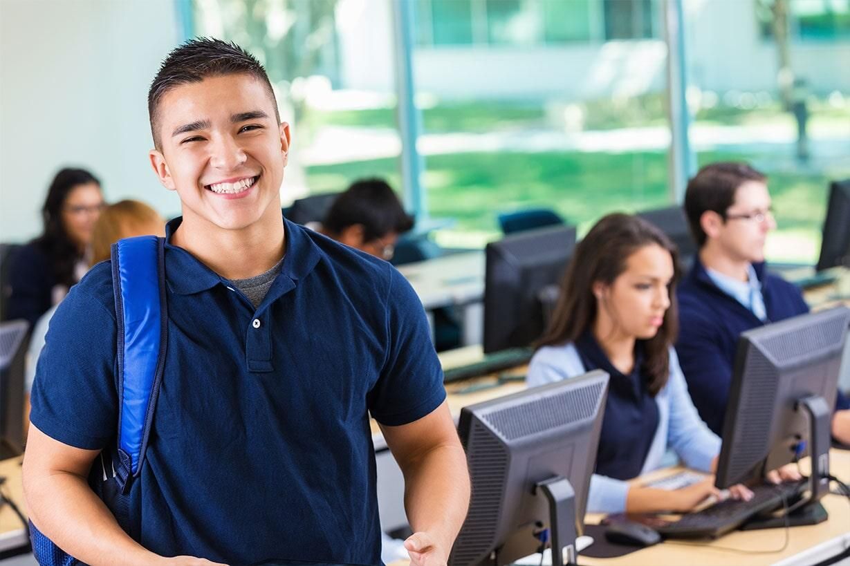 Un grupo de estudiantes está sentado frente a monitores de computadora en un salón de clases.