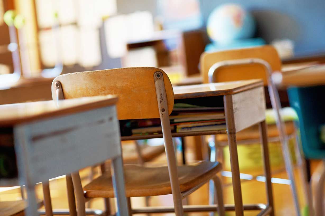 Un salón de clases con escritorios y sillas vacíos y un globo terráqueo al fondo.