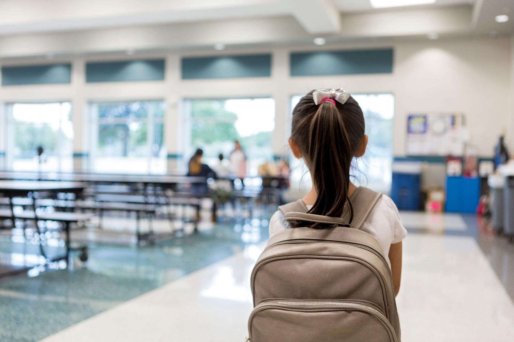 Una joven con una mochila está parada en la cafetería de una escuela.