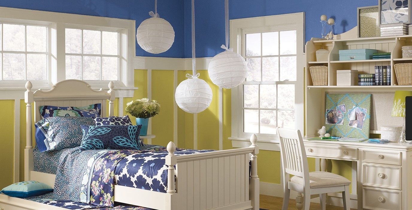 Bright bedroom with white furniture, blue bedding, and sunlit windows, accented by hanging paper lanterns