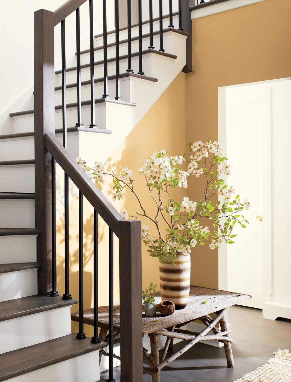 Staircase corner with a small table holding a potted flowering branch and a white cabinet nearby.