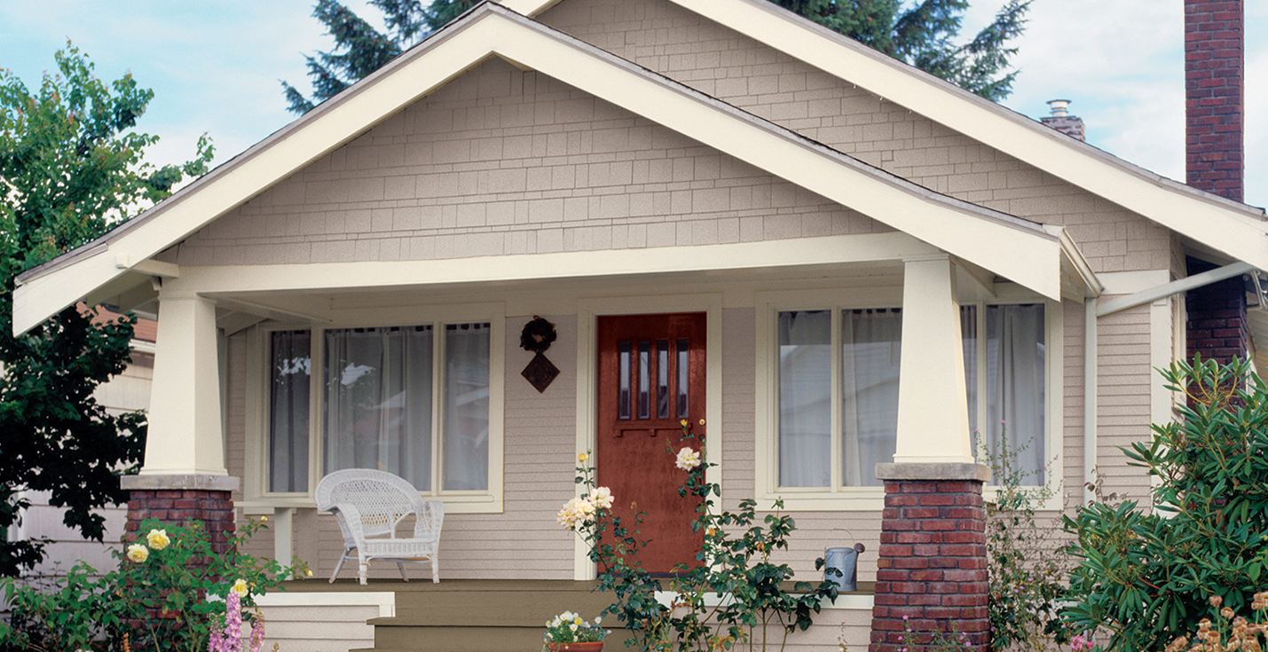 Small beige bungalow with a front porch, white trim, brick columns, and a red front door.
