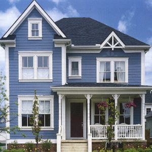 Blue two-story house with white trim, porch, and dark roof against a cloudy sky.