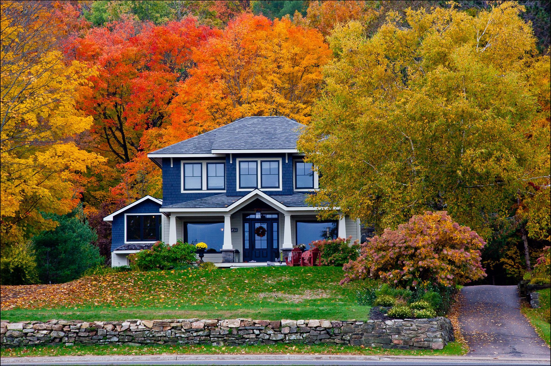 Blue house framed by vibrant autumn trees beside a quiet road