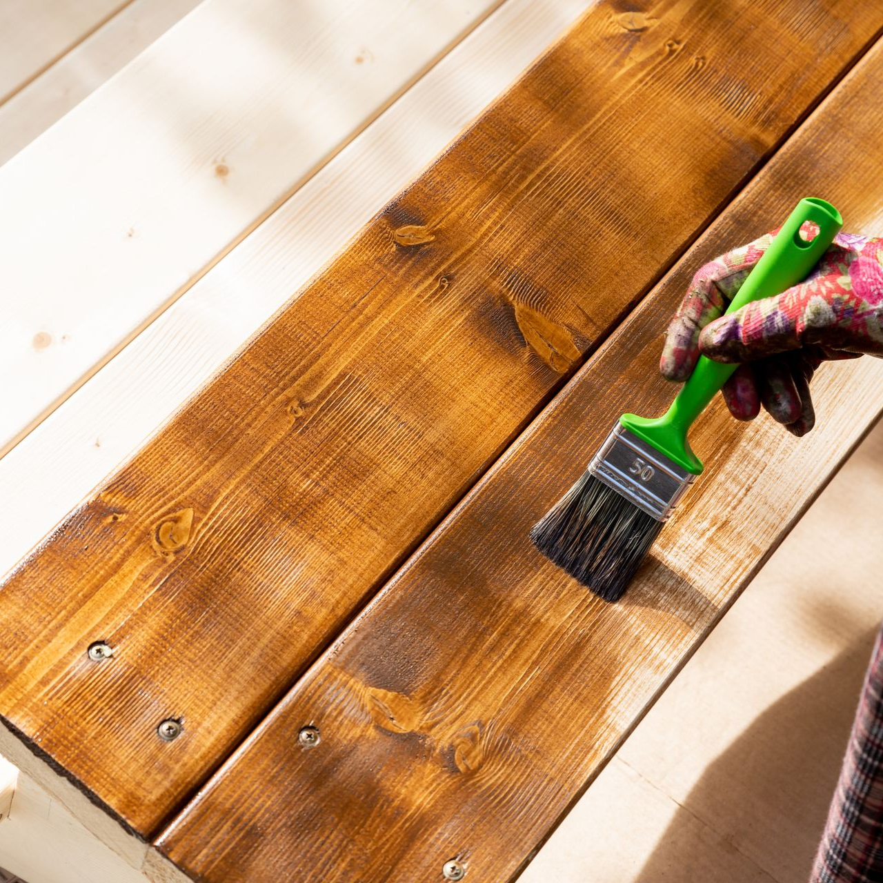Hand with brush applying stain to wooden planks.
