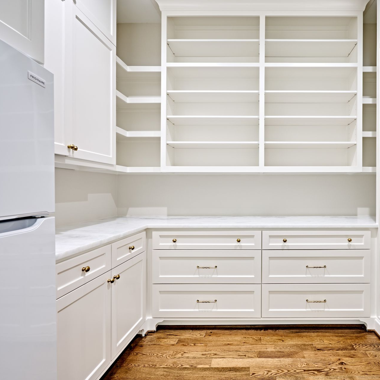 White pantry with shelves, cabinets, drawers, and wooden floor.
