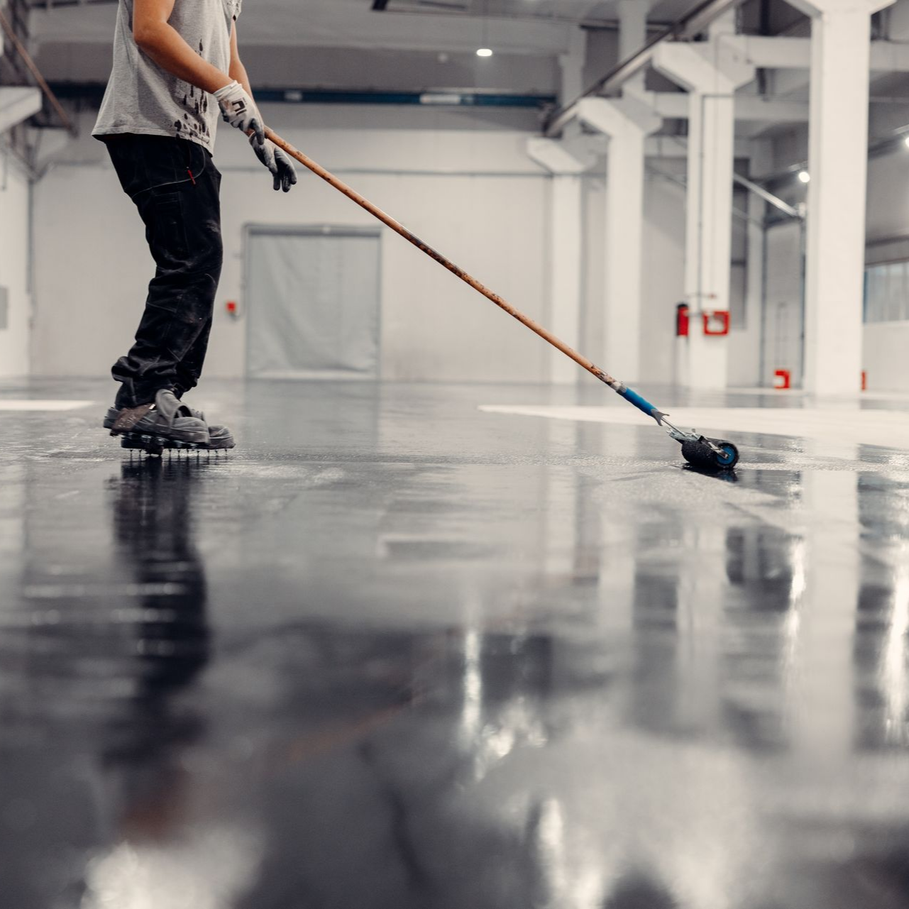 Worker mopping a glossy floor in a bright industrial warehouse