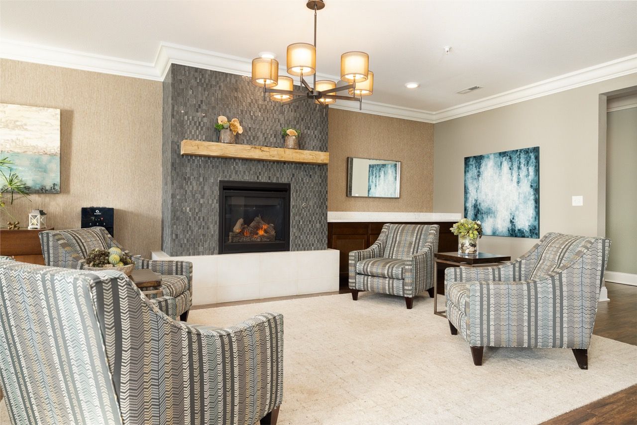 Indoor community lounge with a stone fireplace, four striped armchairs, and decorative art.