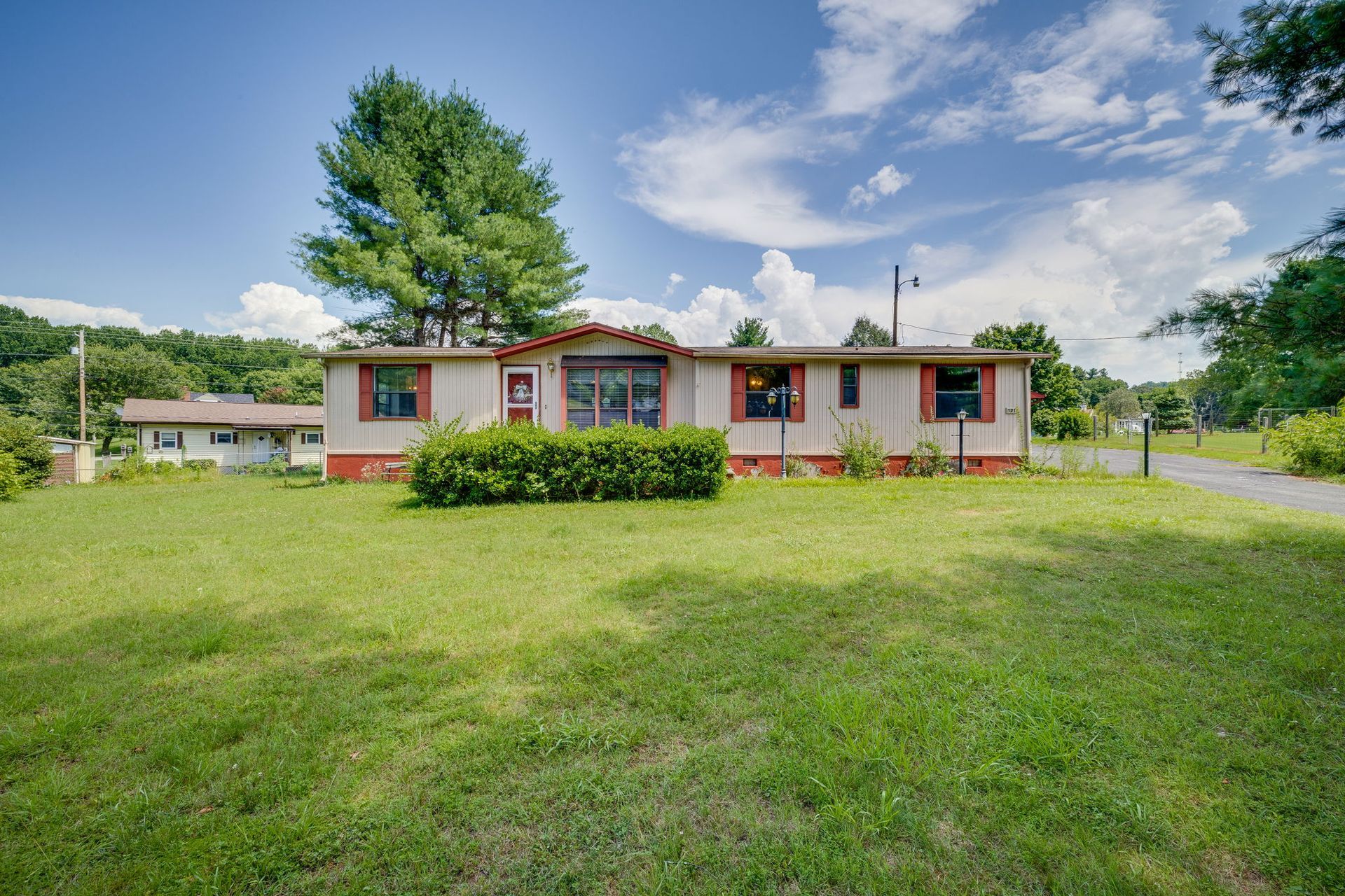 Single-story house with red trim in a grassy yard under a bright blue sky