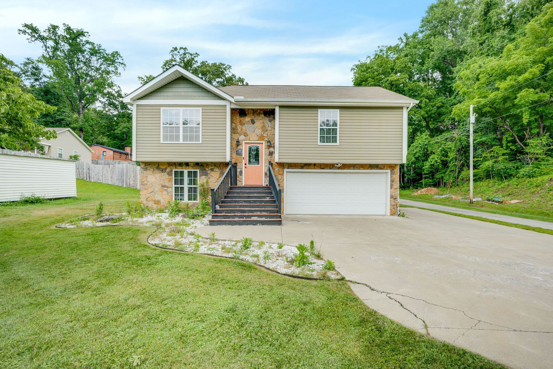 Suburban split-level house with a front deck, garage, and driveway beside a grassy yard and trees