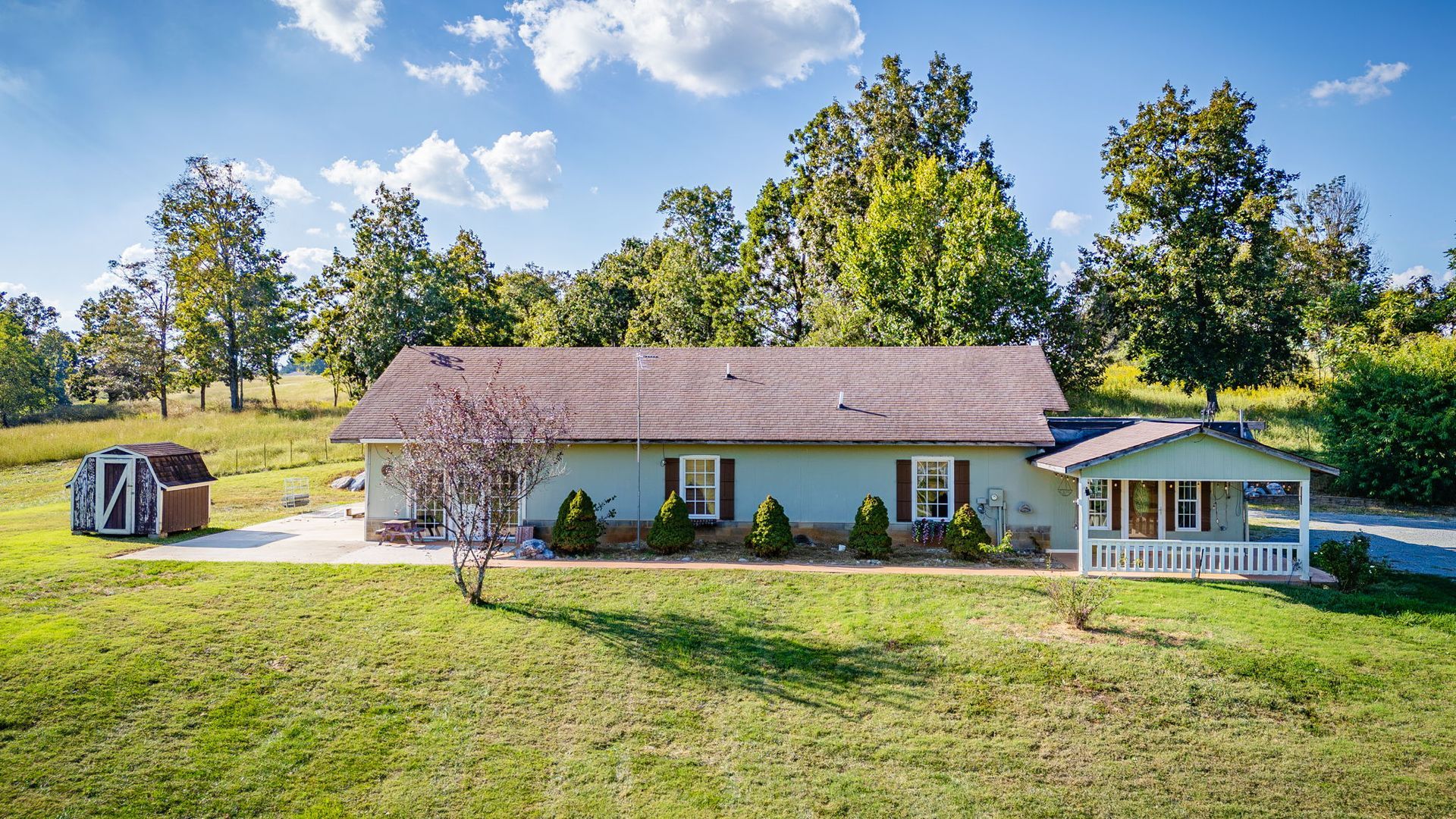 Rural house with a screened porch and gazebo beside a grassy yard and trees on a sunny day