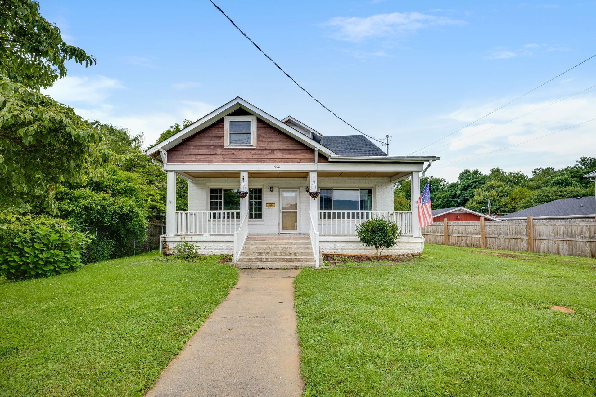 Small white house with front porch, green lawn, and concrete walkway under a blue sky