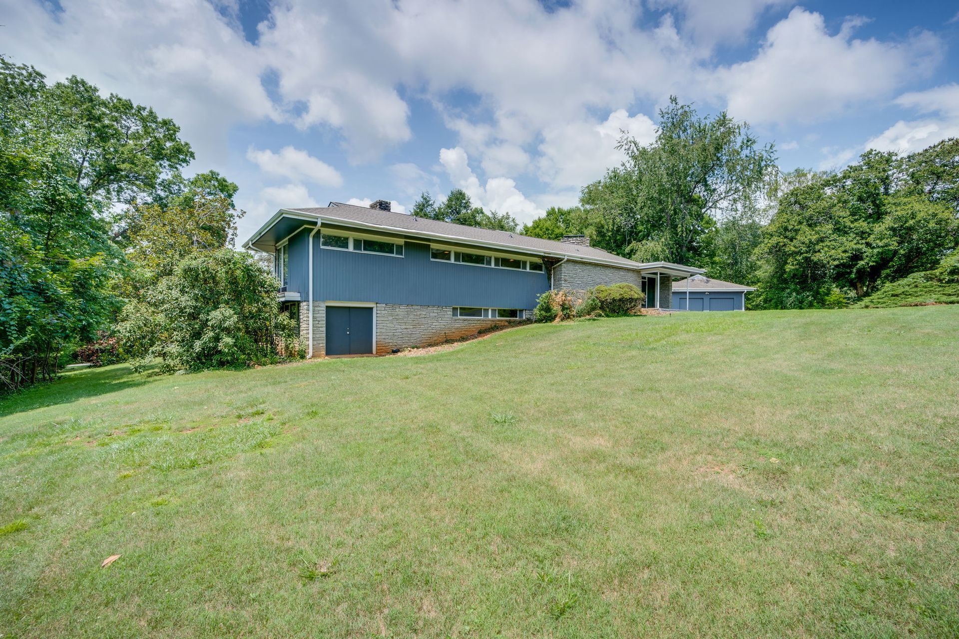 Blue house on a grassy hillside with trees and a partly cloudy sky