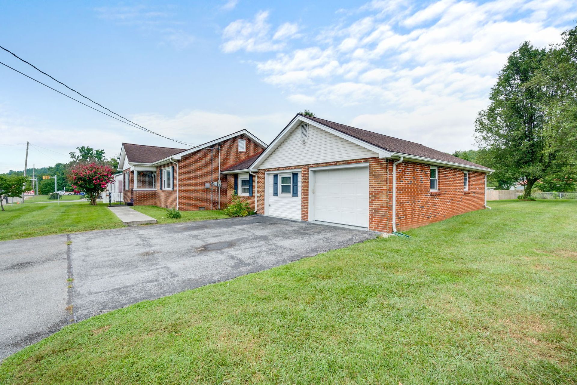 Single-story brick house with white garage door, driveway, and grassy front yard under a partly cloudy sky