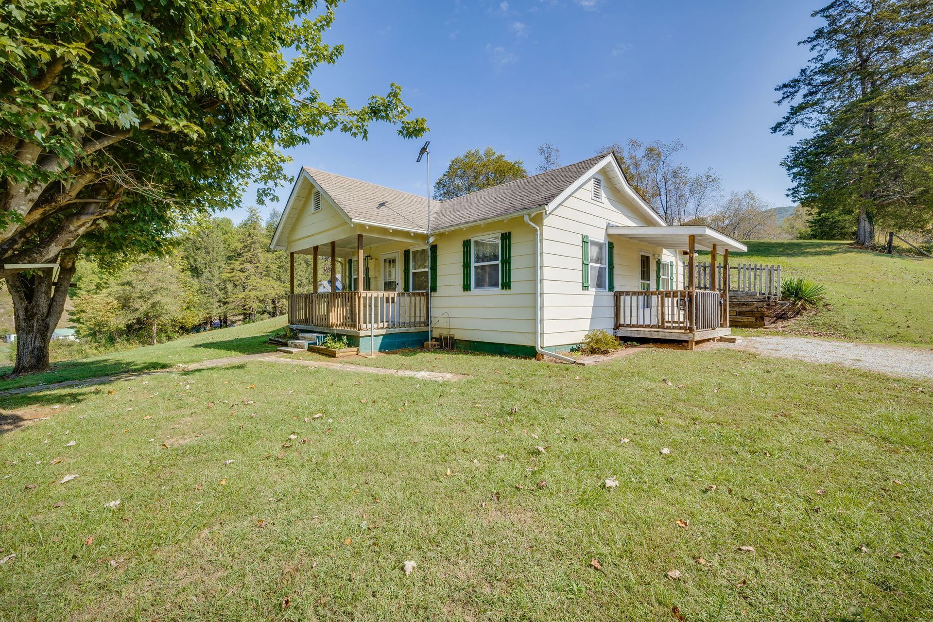 Small white house with a front porch on a grassy lot, surrounded by trees under a clear sky