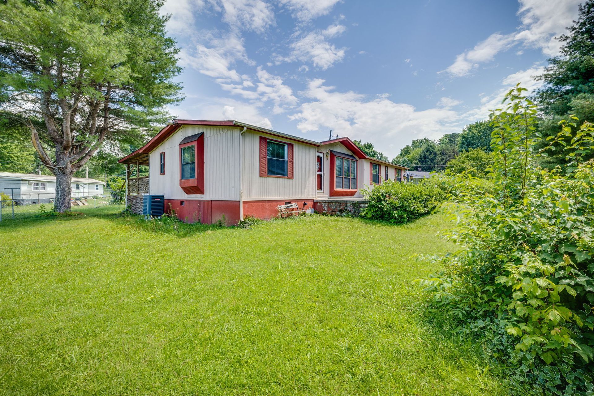 Small white house with red trim in a grassy yard under a partly cloudy sky