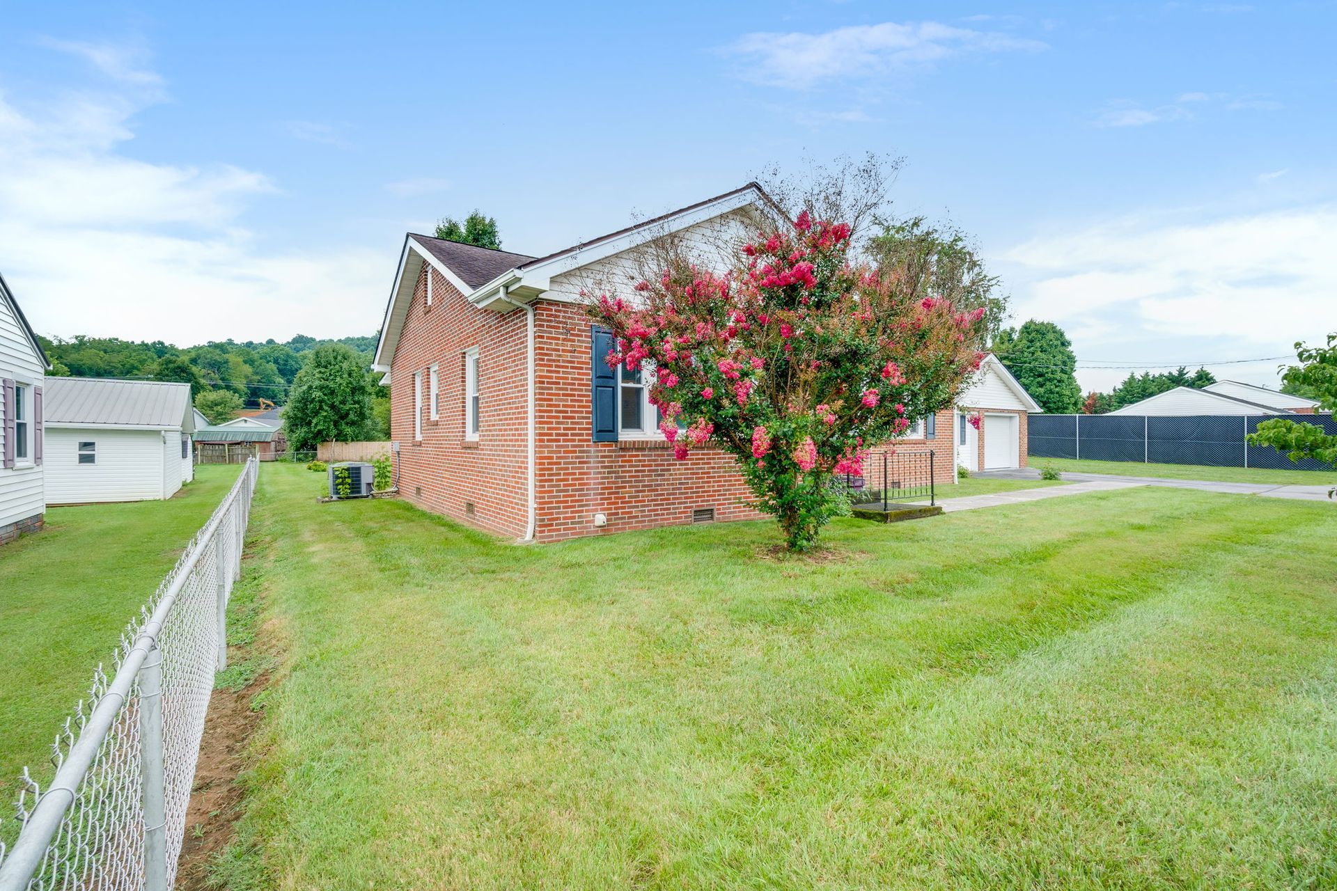 Brick house with a pink-flowering tree and wide green lawn under a blue sky