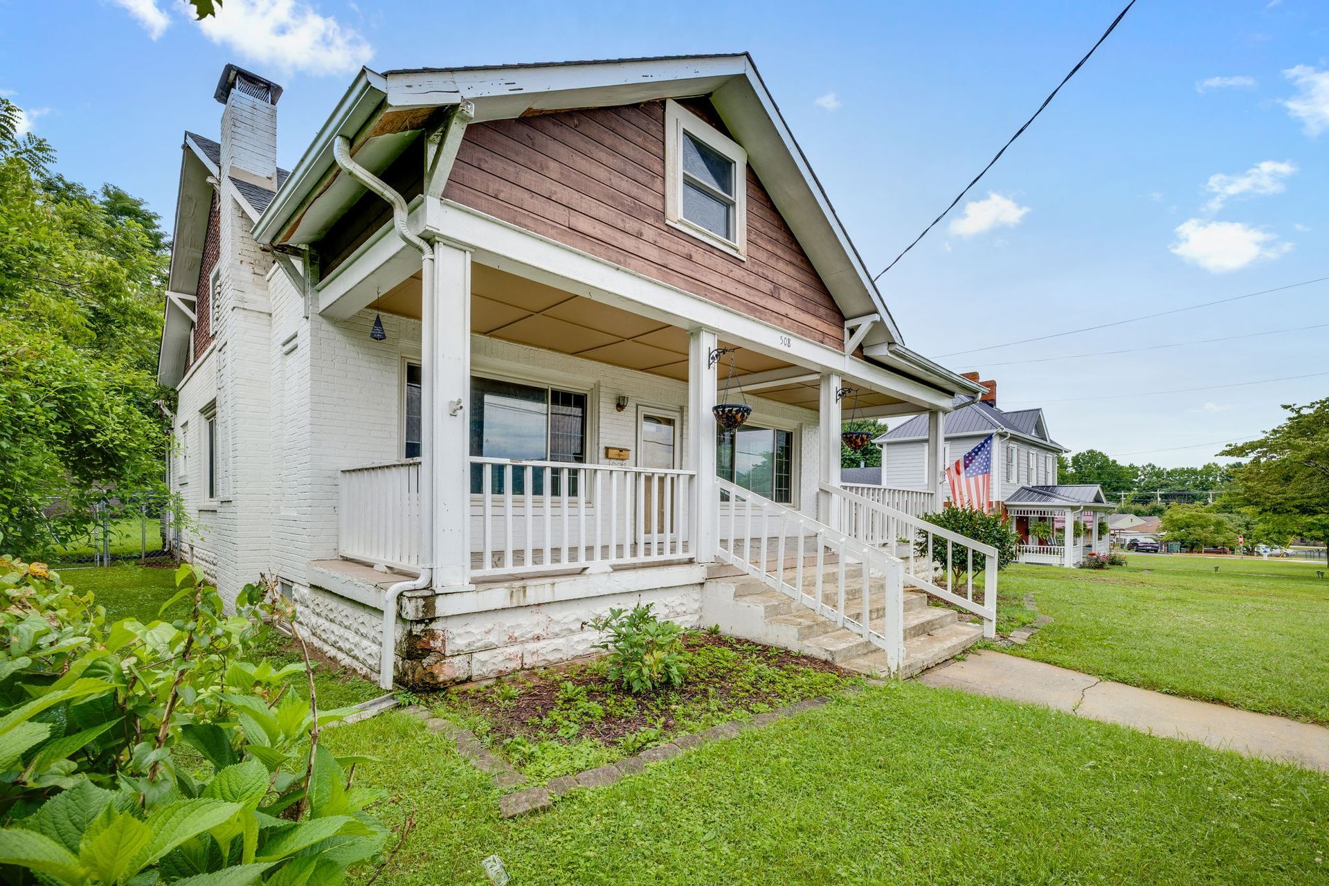 White house with porch, steep roof, and front lawn on a sunny day