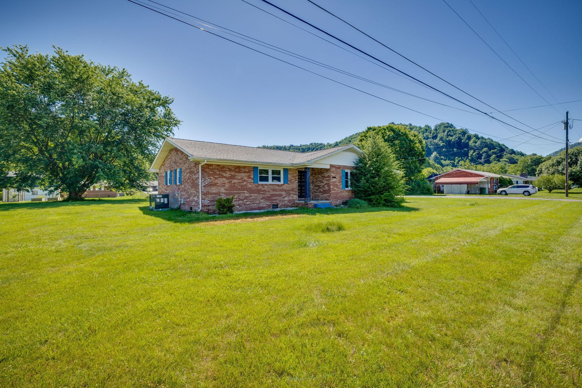 Single-story brick house with blue shutters on a large grassy lot under a clear sky