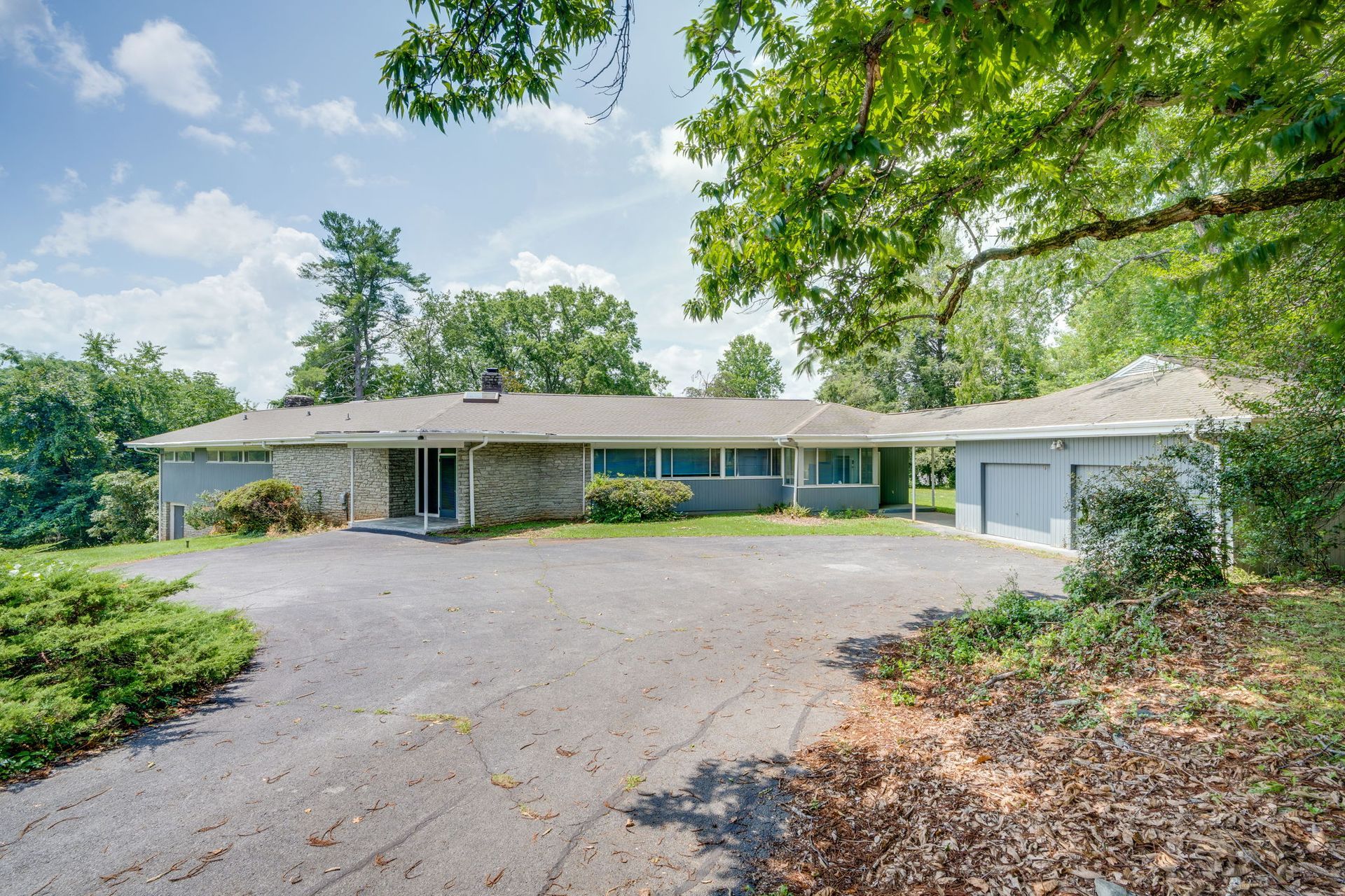 Single-story house with a curved driveway, trees, and a large front porch.