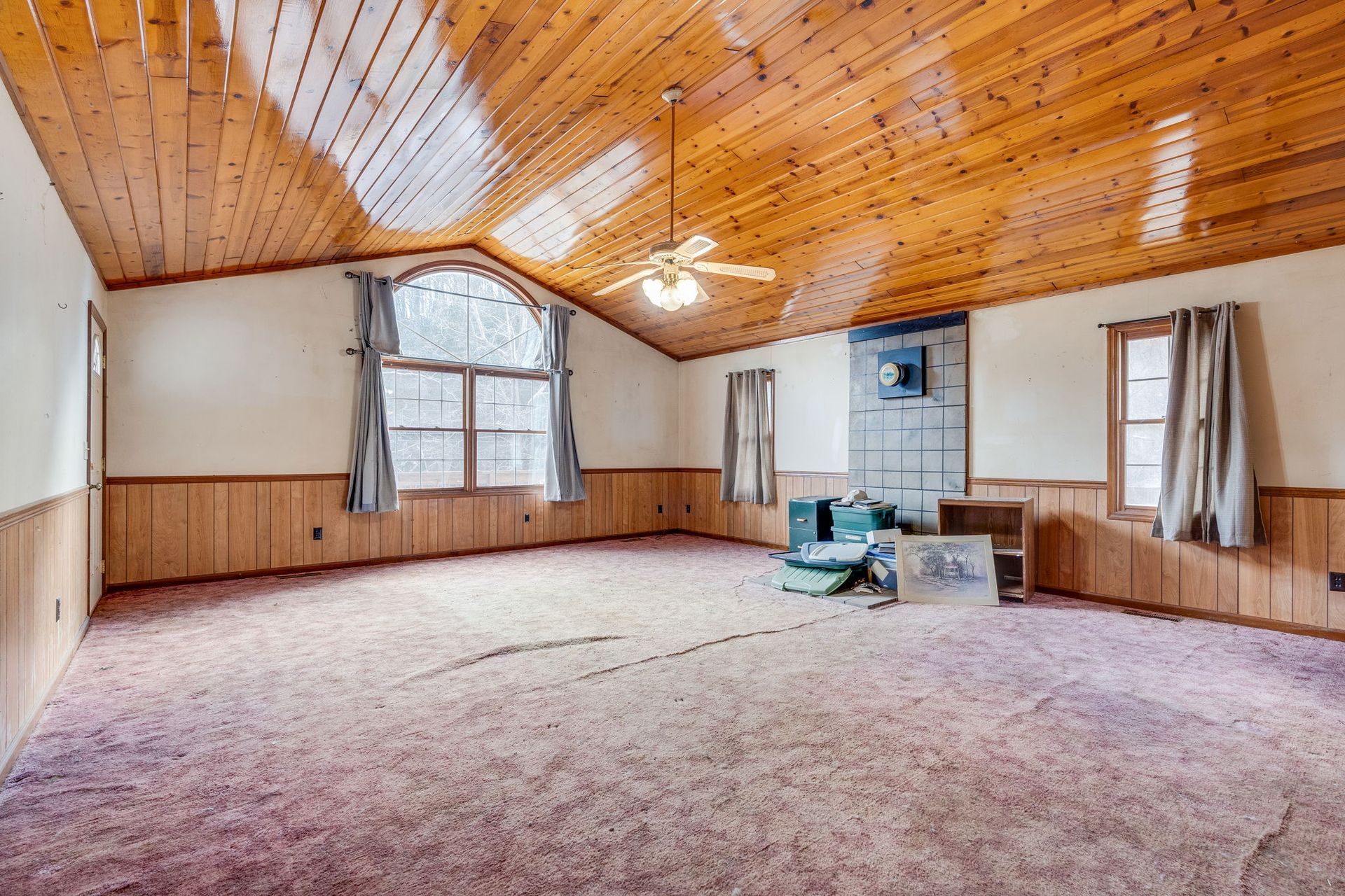 Empty living room with wood paneling, sloped wood ceiling, carpet, and windows.