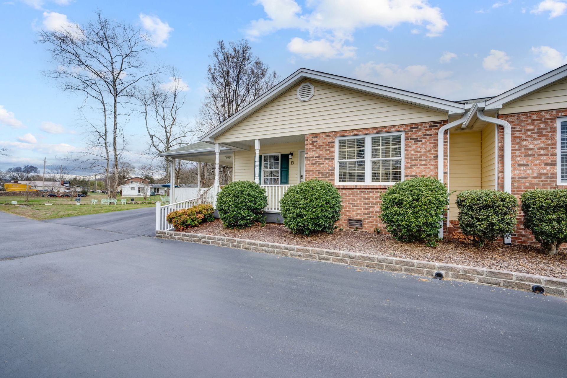 A one-story brick and tan siding house with a covered entryway, large front windows, and landscaped shrubs.