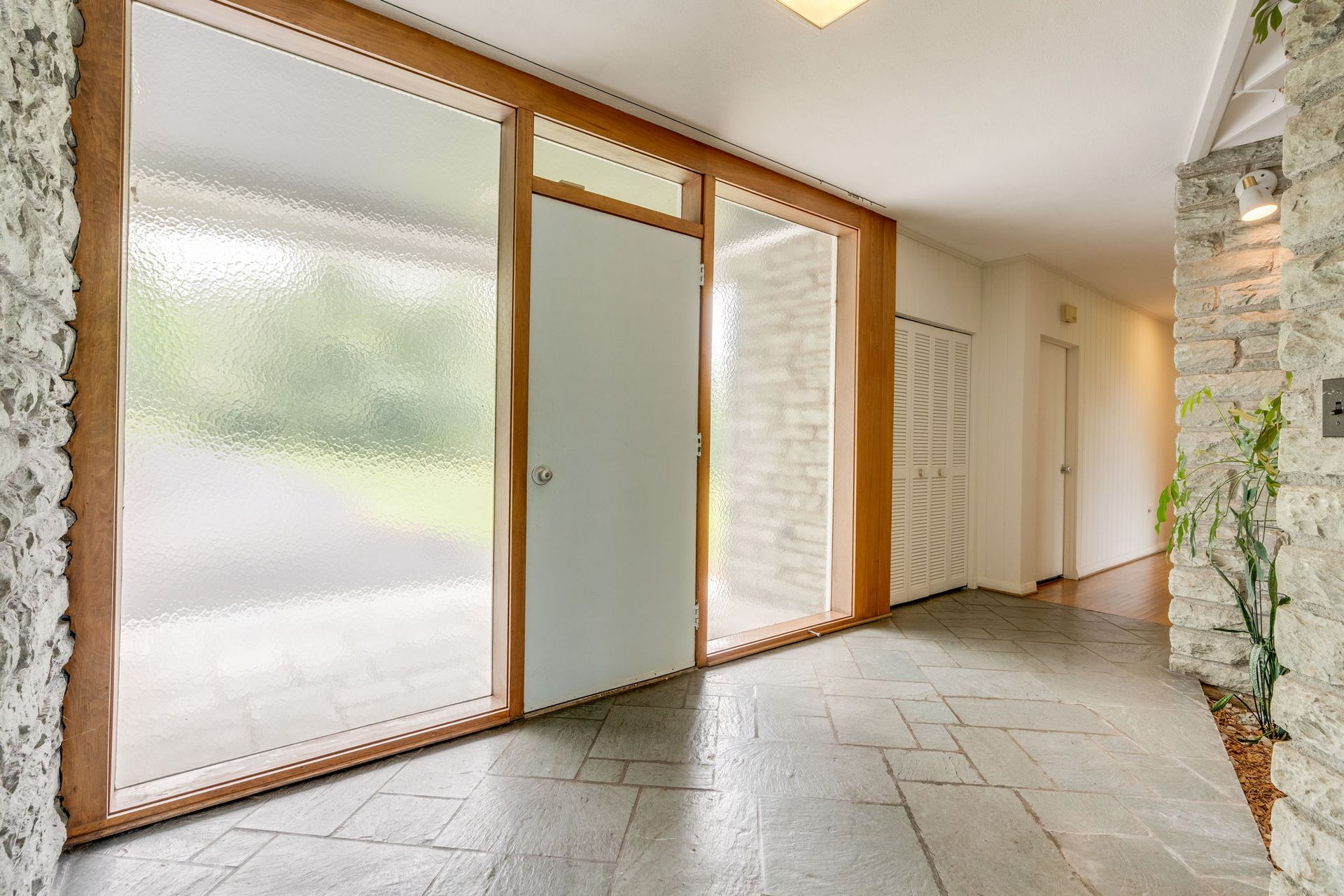 Modern foyer with frosted glass doors, tiled floor, stone wall, and skylight overhead
