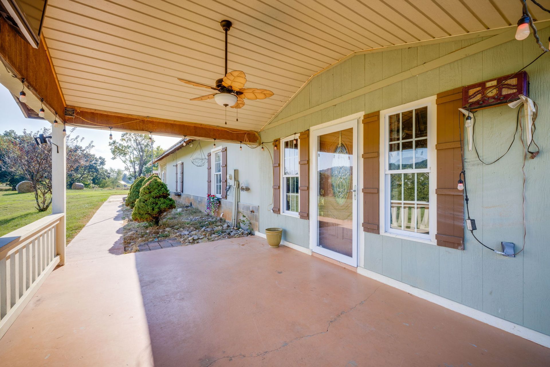 Covered front porch with ceiling fan, double glass doors, and light green siding overlooking a grassy yard