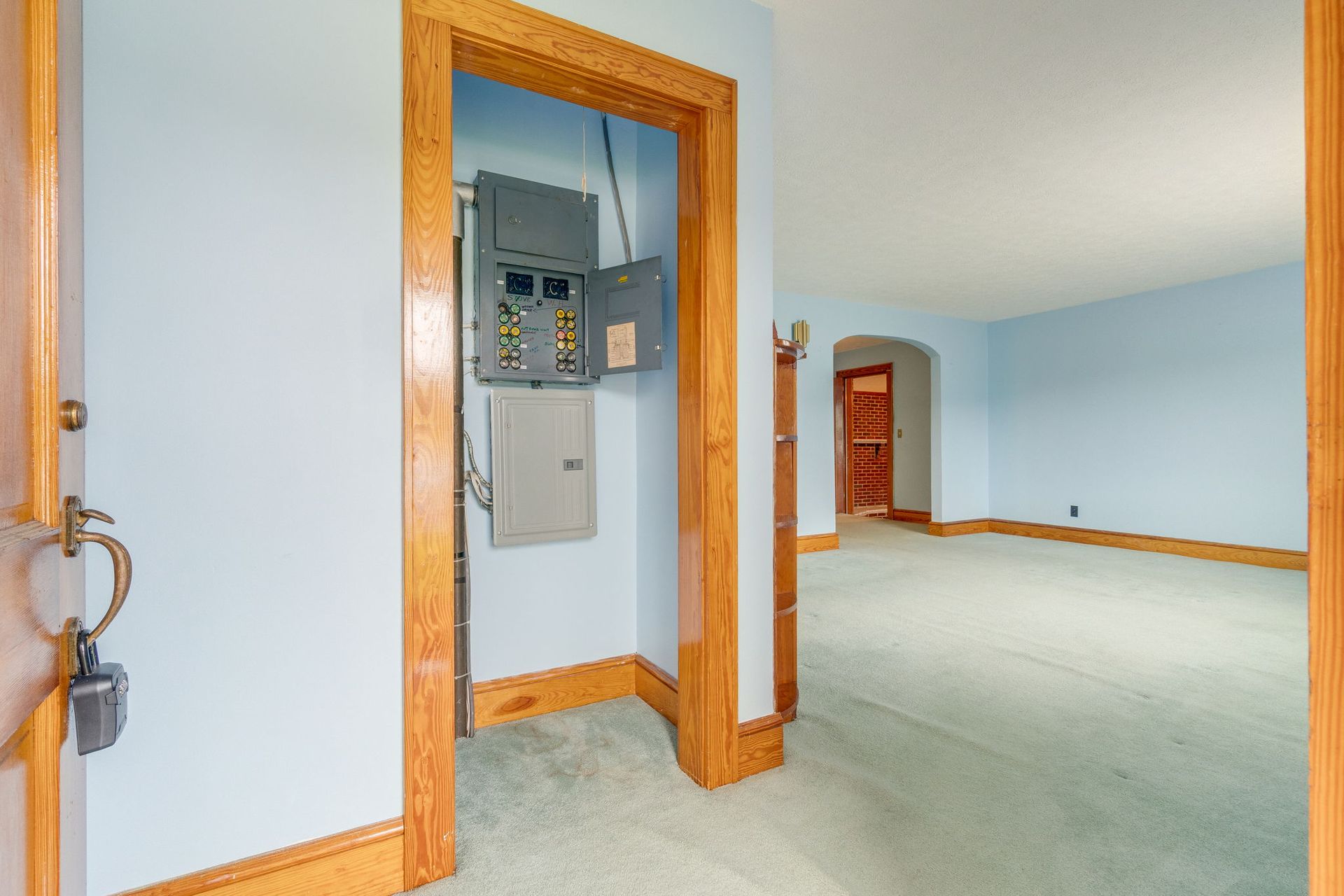 Empty hallway with blue walls, green carpet, and an open electrical panel framed by wood trim