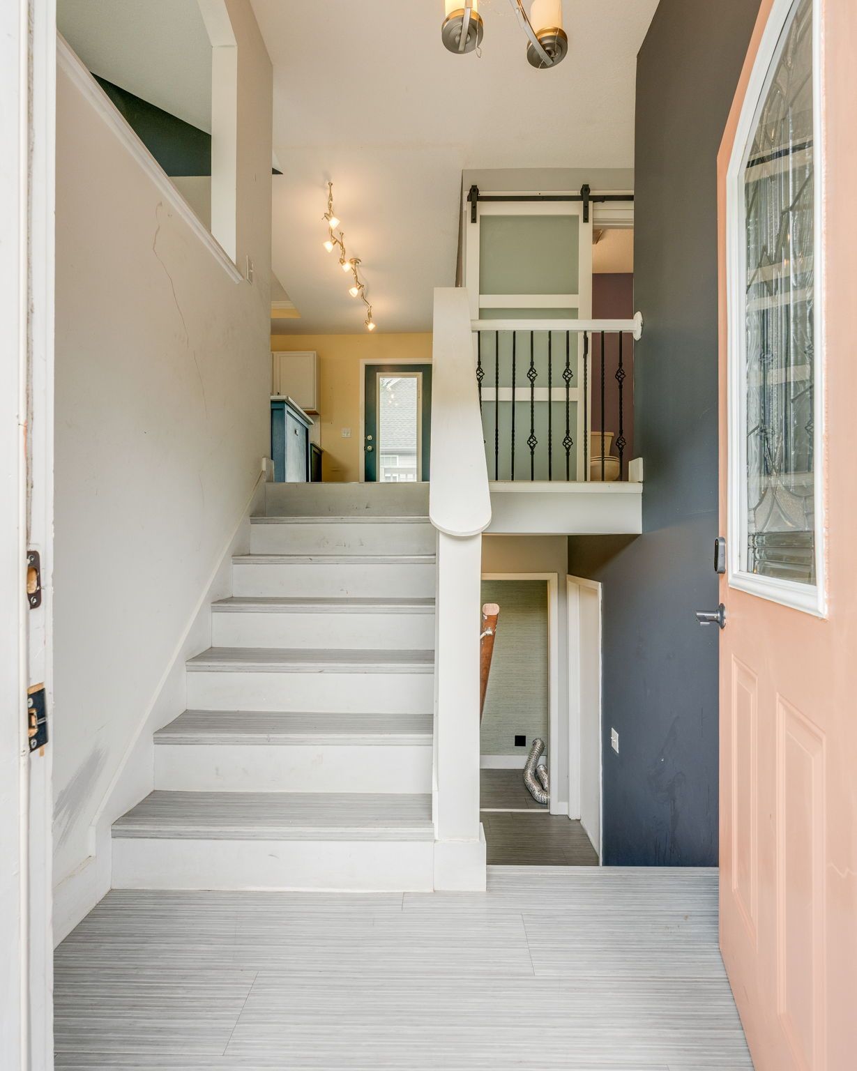 Bright entryway with white stairs, gray walls, and an open peach-colored front door.