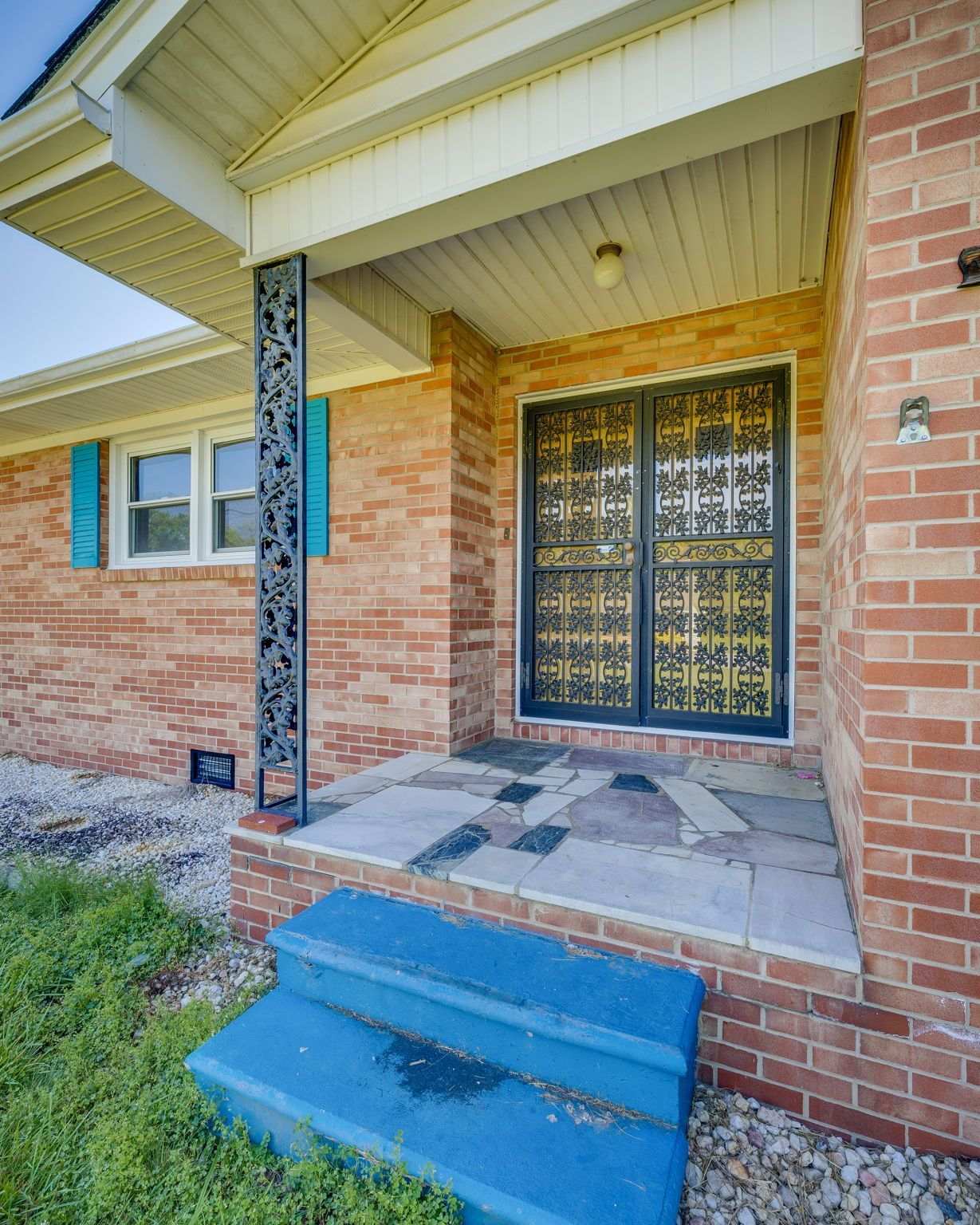 Brick house front porch with blue steps, tiled entry, and decorative black double doors