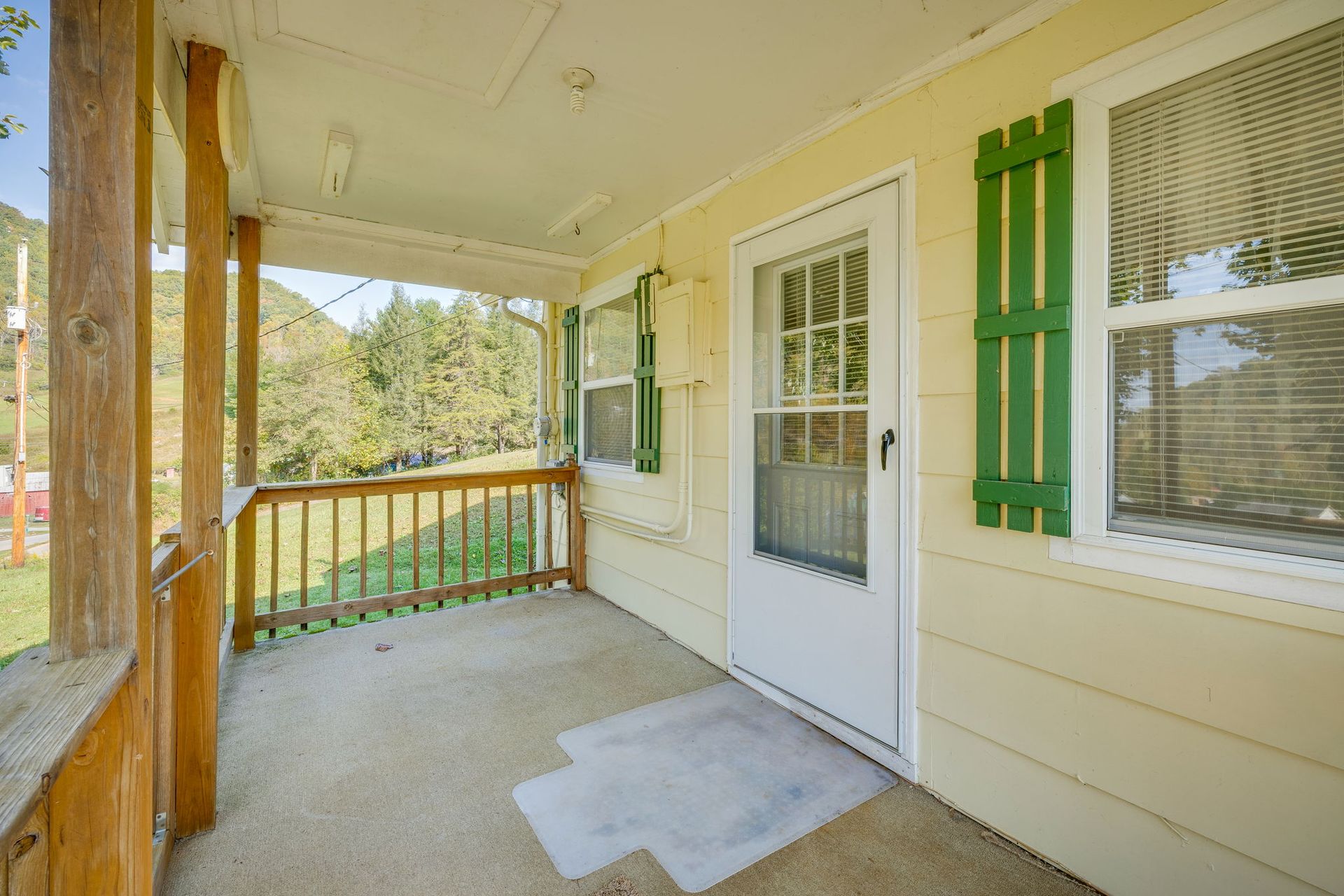 Front porch with white siding, green shutters, a screen door, and wooden railings.