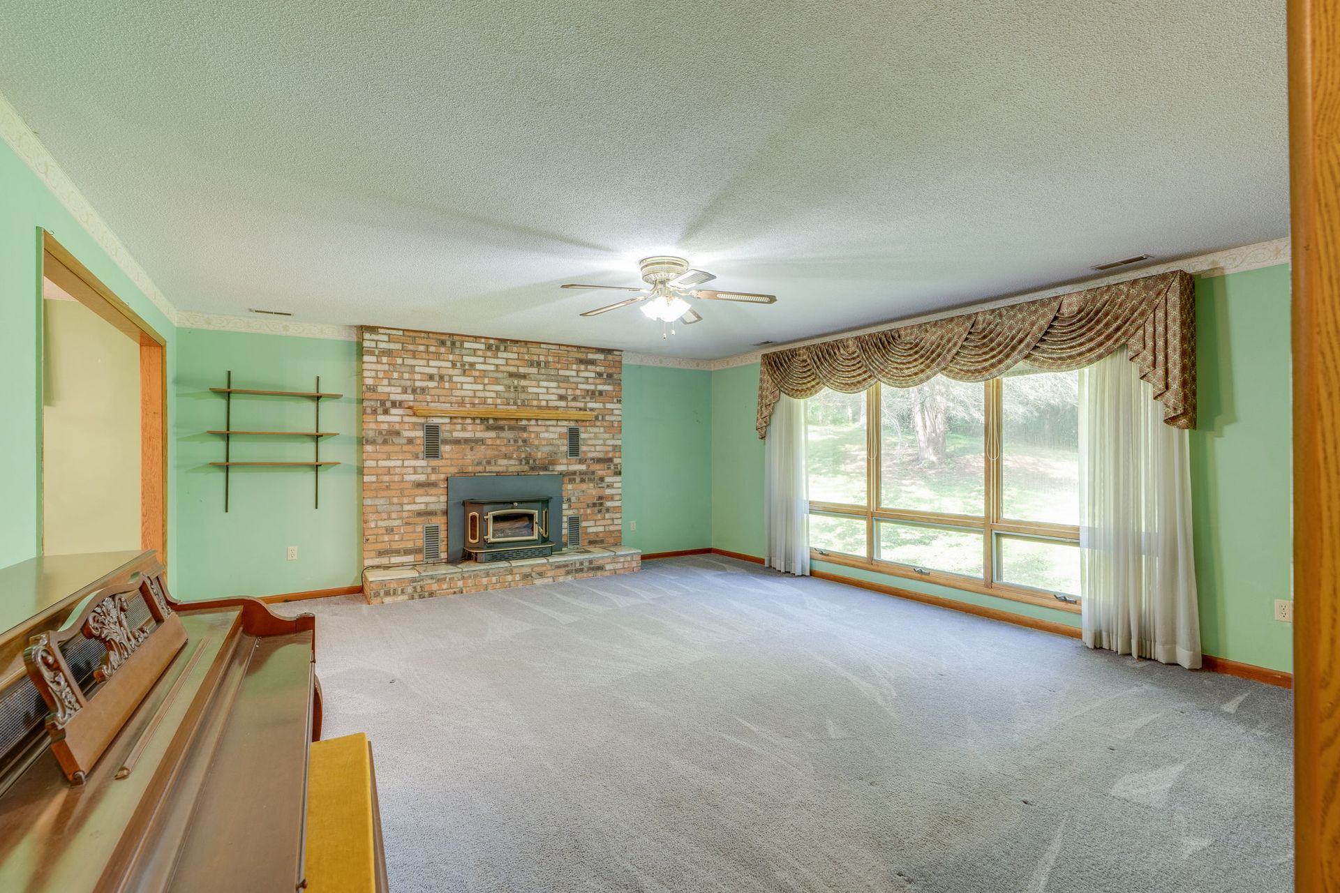 Empty living room with green walls, stone fireplace, carpet, and large windows with drapes
