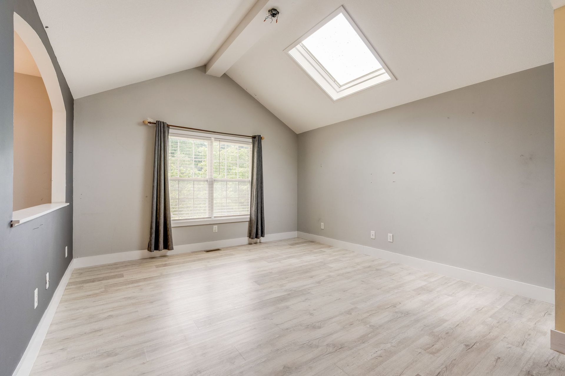 Empty gray bedroom with vaulted ceiling, skylight, and a window with curtains