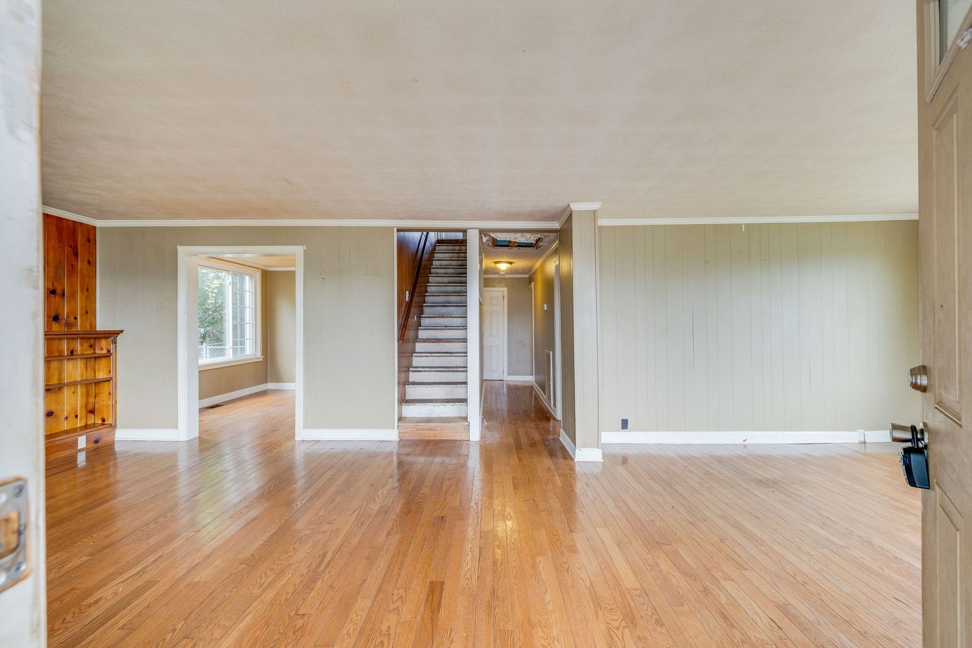 Empty living room with hardwood floors, beige walls, and a staircase in the center.