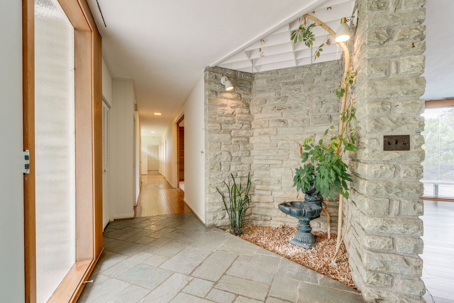 Bright stone hallway with tiled floor, doorway, and potted plants in a modern home entryway.