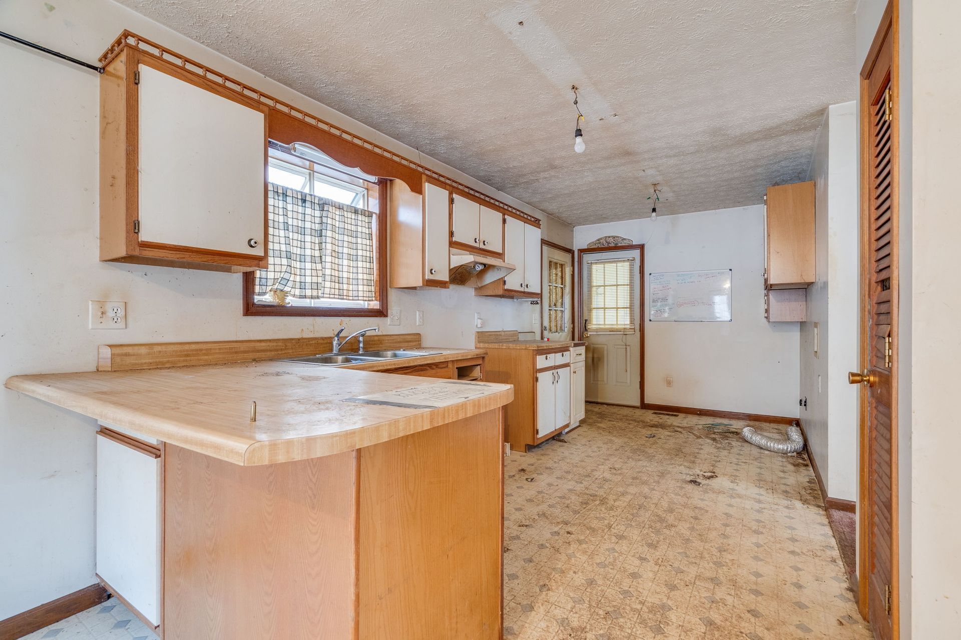Dilapidated kitchen with white cabinets, light wood counters, and peeling floor.