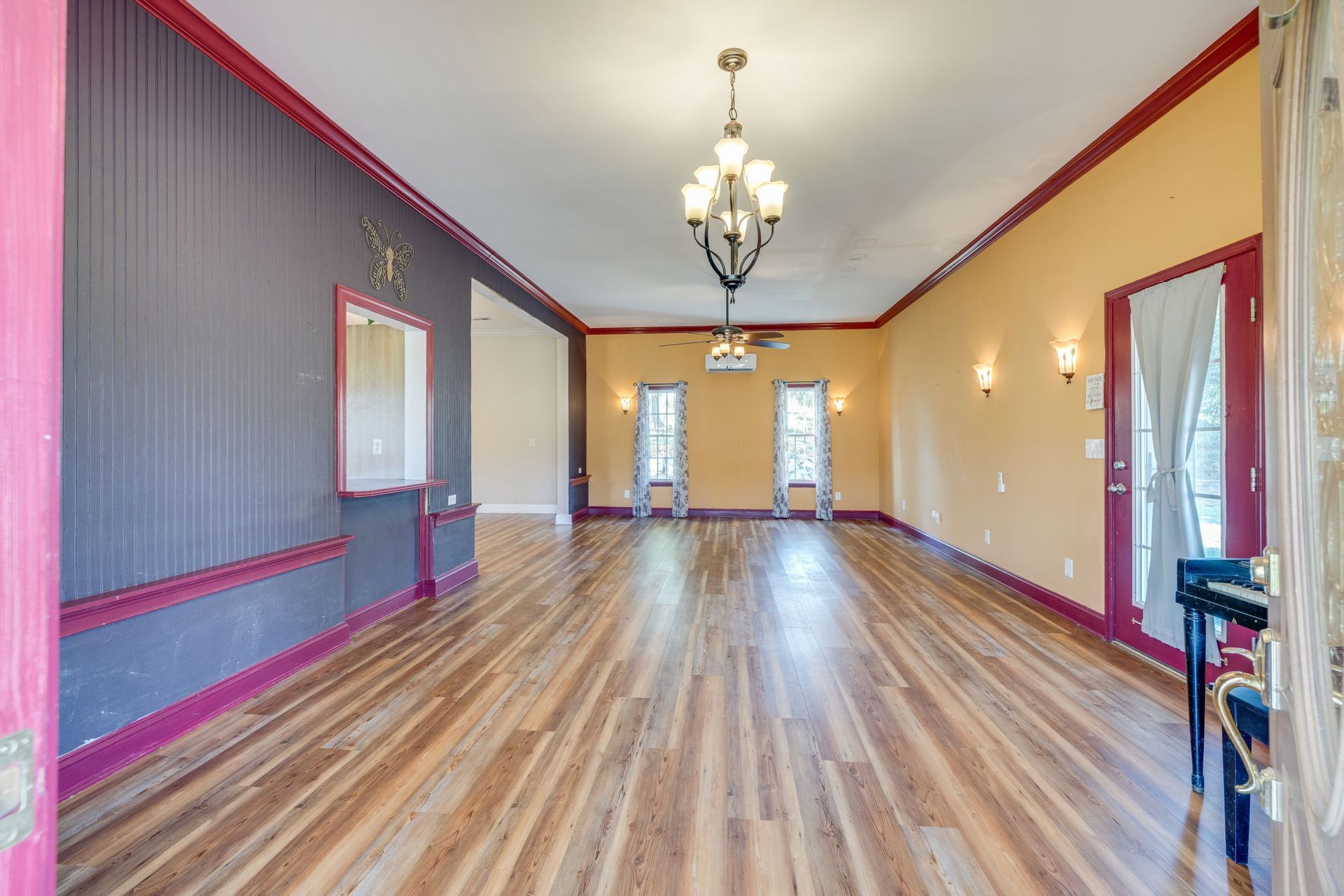 Empty long hallway with wood floors, red trim, mirrors, and chandeliers