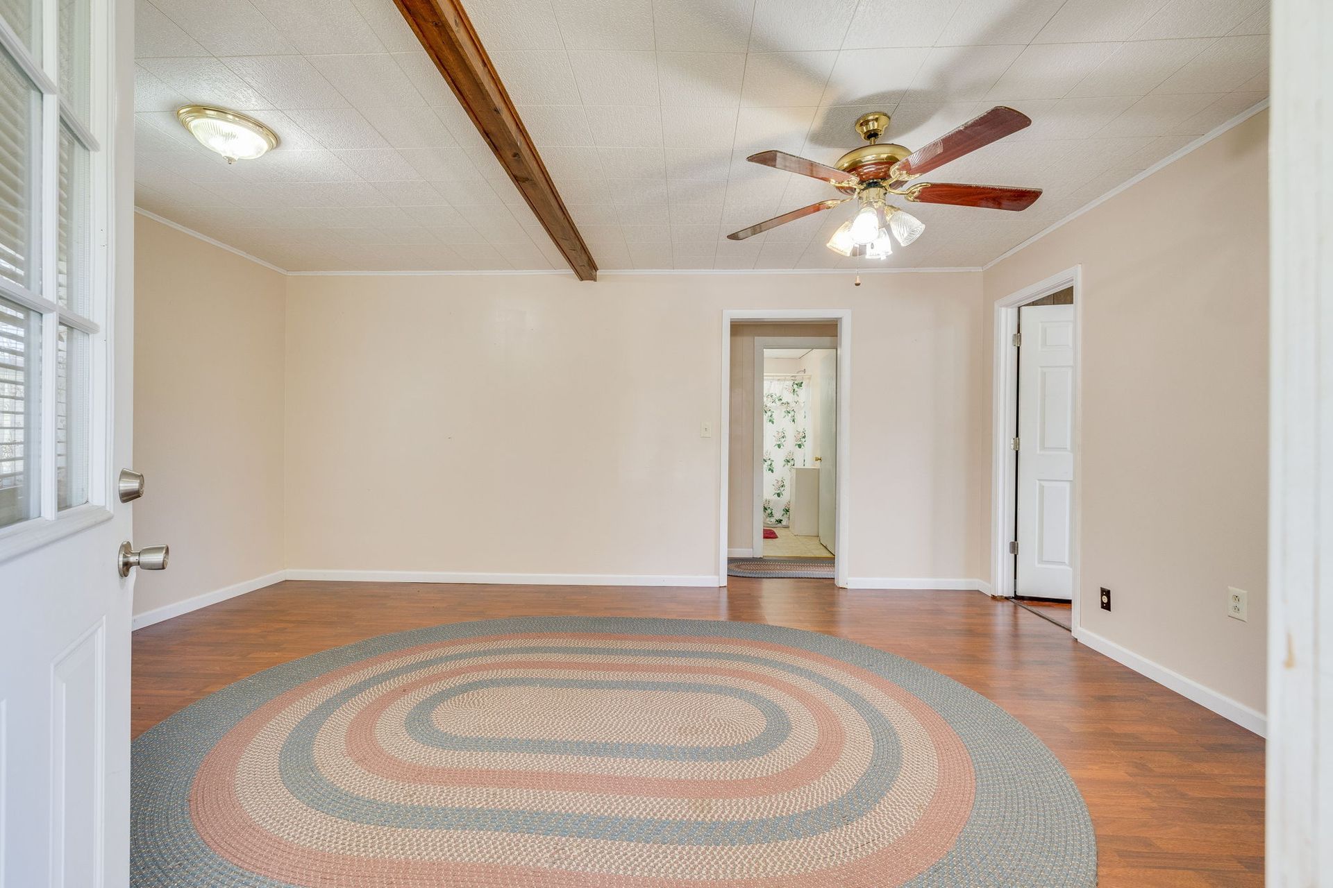 Empty living room with hardwood floors, ceiling fan, and a large round rug.