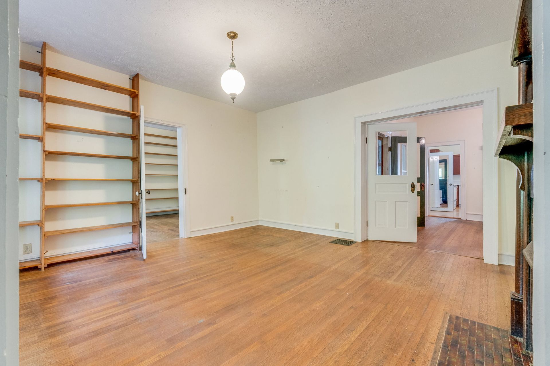 Empty room with hardwood floors, cream walls, open doorway, and built-in wooden shelves along the left wall