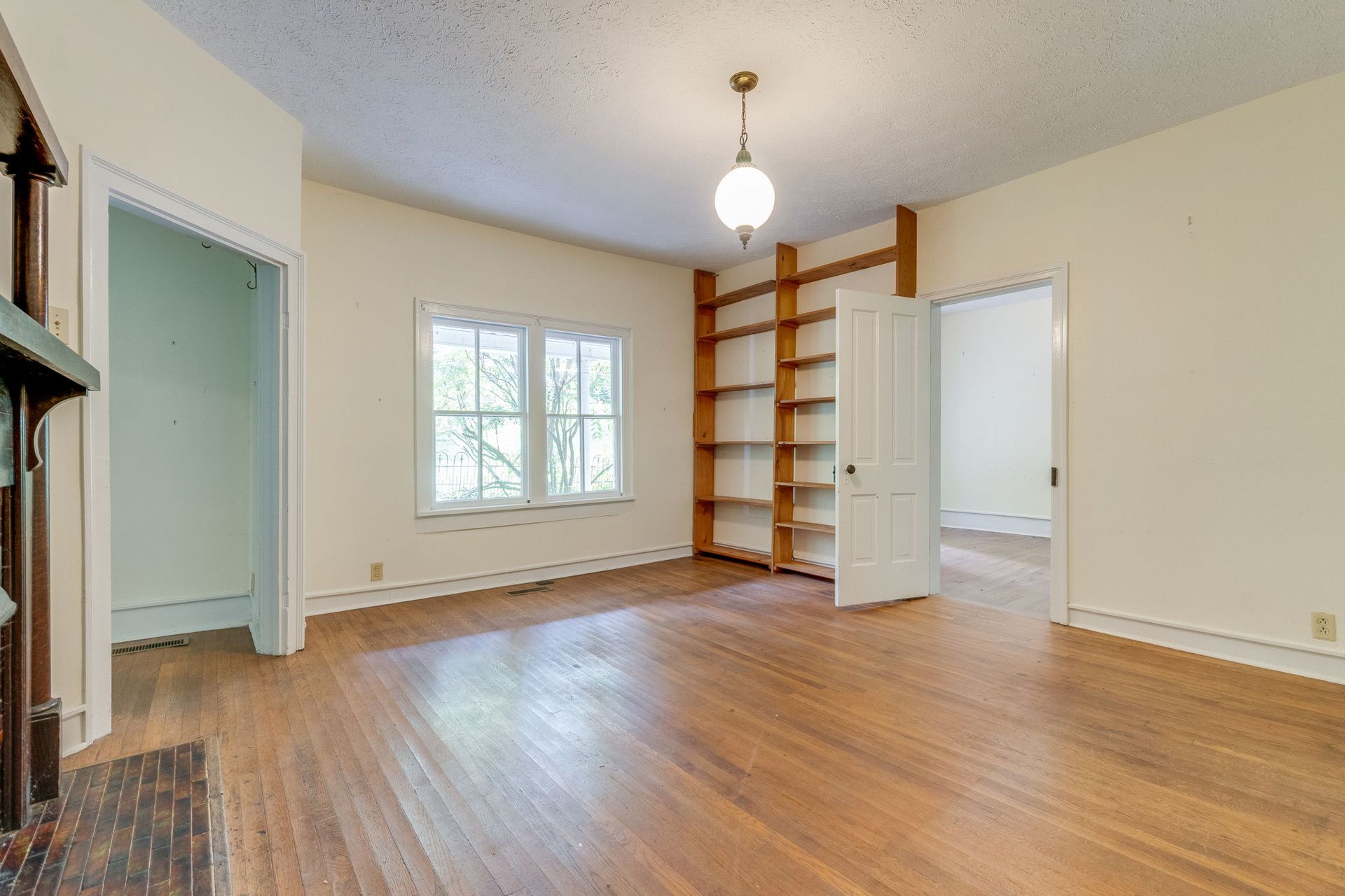 Empty room with hardwood floors, white walls, window, and built-in wooden shelves.