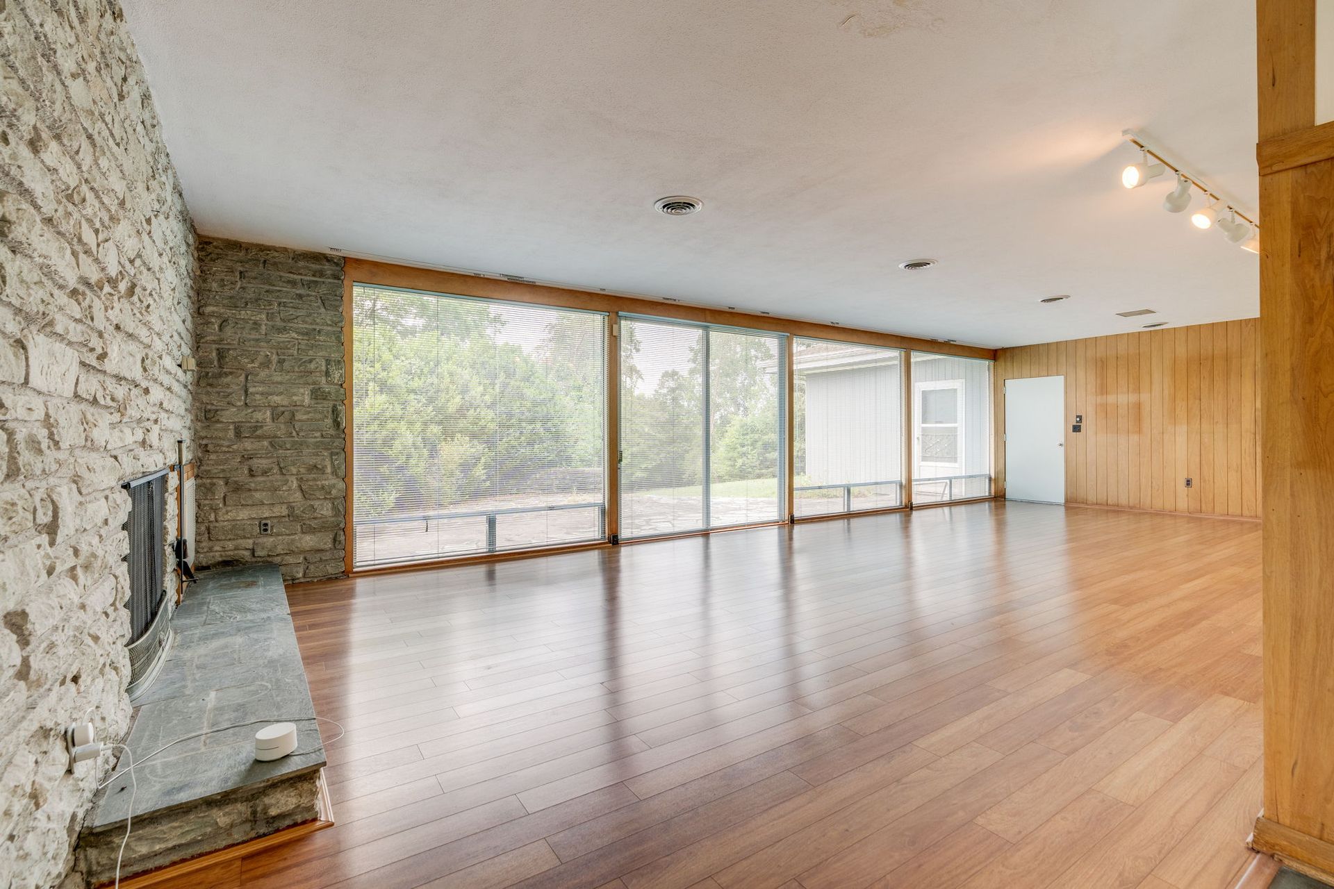Empty living room with stone wall, wood floors, and large sliding glass doors opening to a view outside