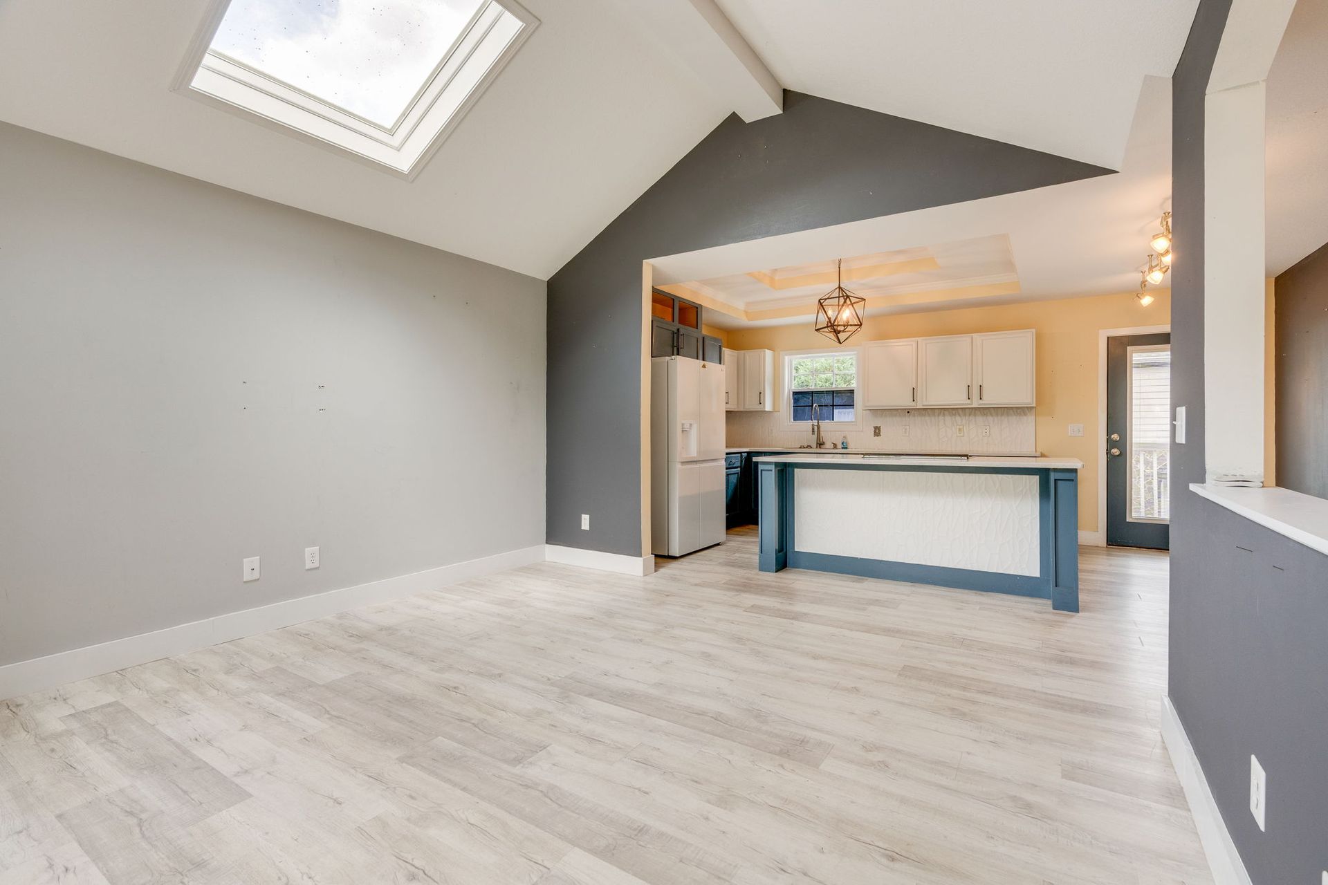 Empty open-plan living room with vaulted ceiling skylight, gray walls, and a kitchen island in back