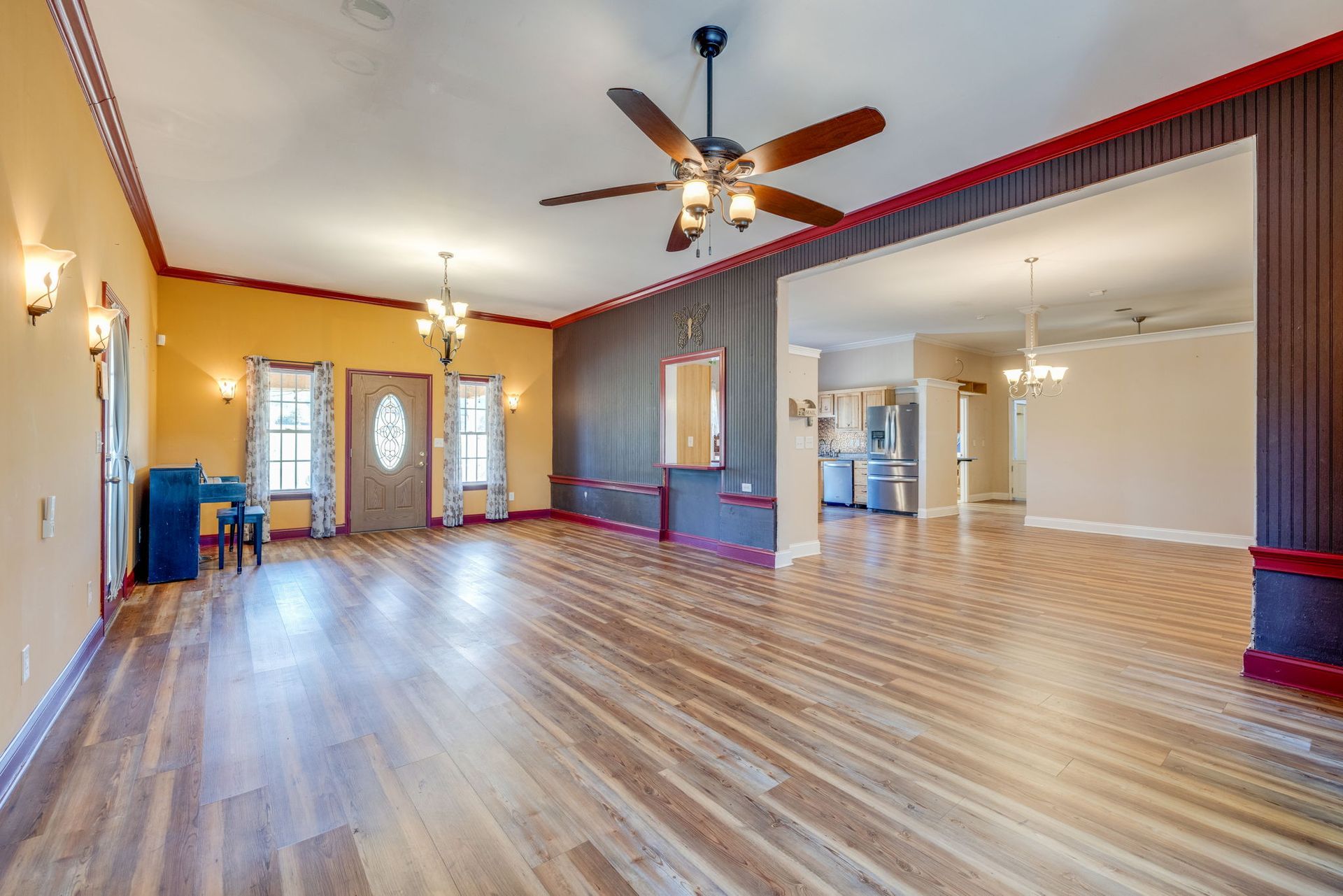Spacious empty living room with wood floors, ceiling fan, and open archway to a kitchen.