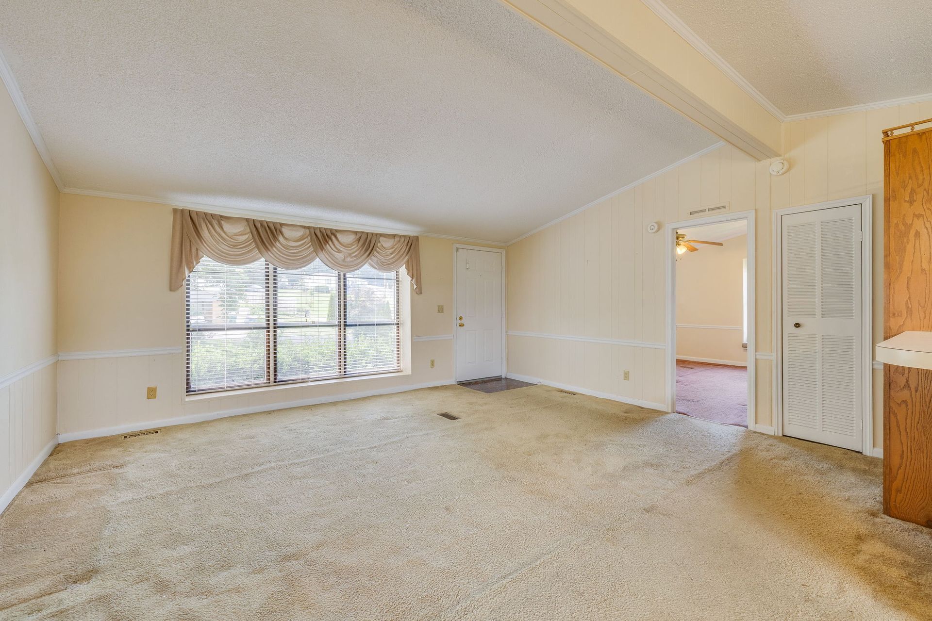 Empty beige carpeted living room with large window and doorway to adjacent room