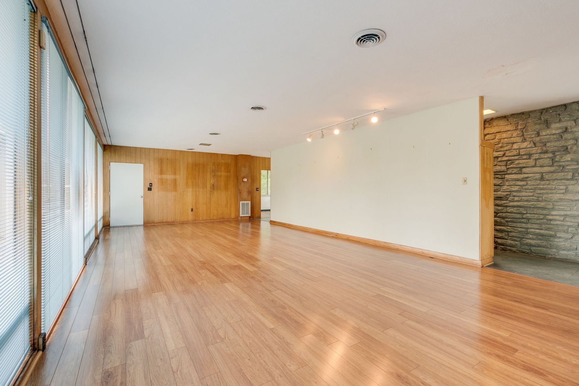 Empty modern room with wood floors, large windows, white walls, and a stone accent wall