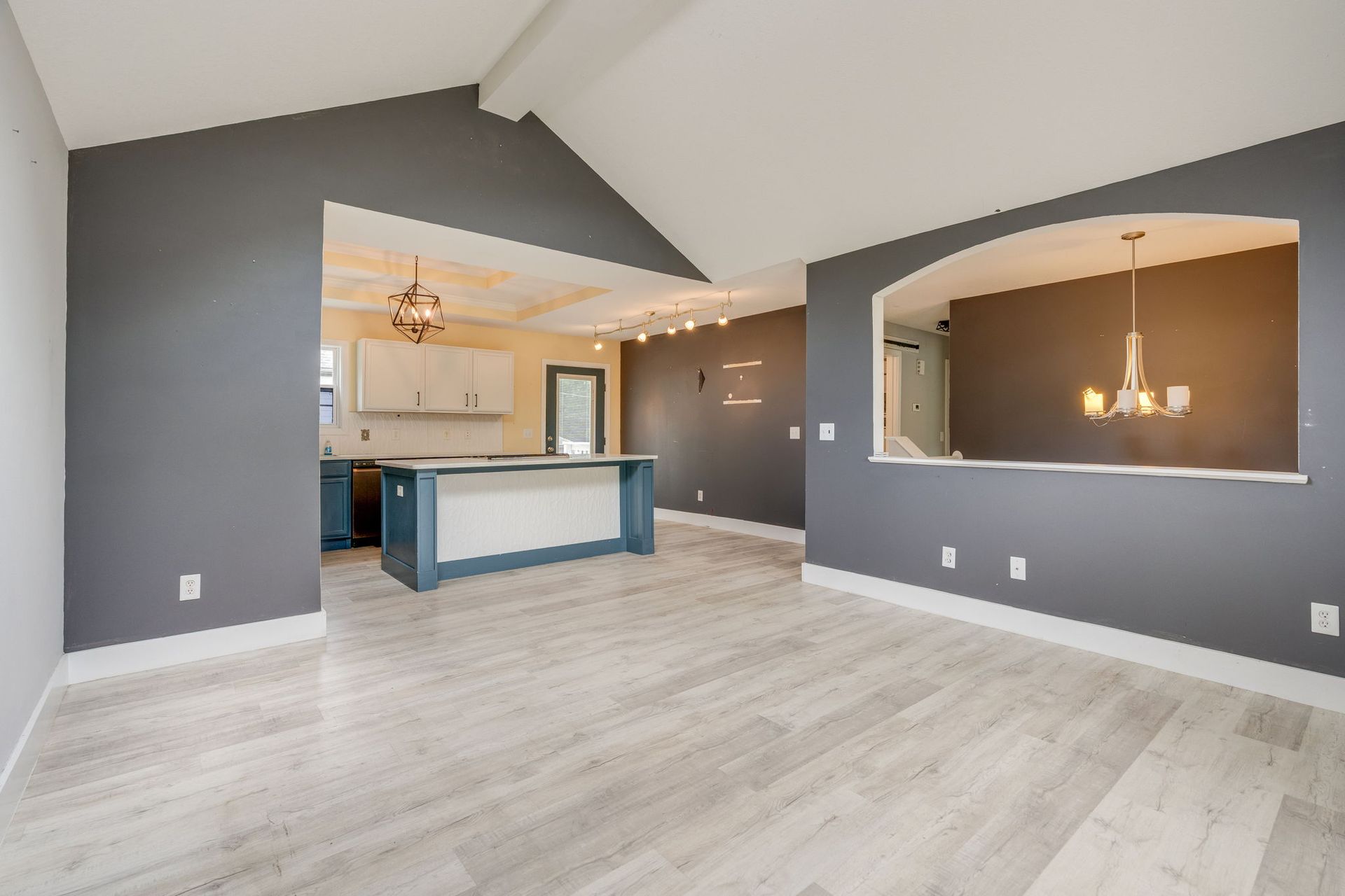 Empty modern open-concept living area with gray walls, light wood floors, and a kitchen pass-through.